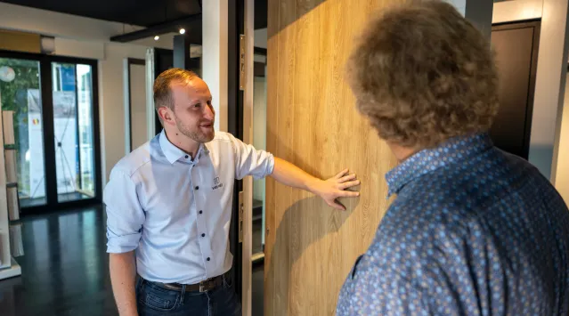 Verkoper Van Van Heegh geeft uitleg in de showroom aan een klant. Hij staat naast een deur. 