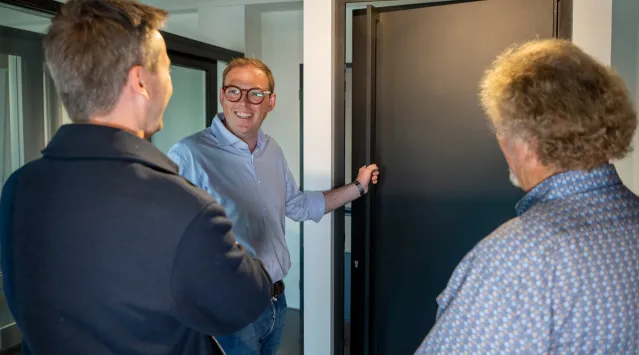 verkoper geeft uitleg over deuren in de showroom met 2 mensen voor hem